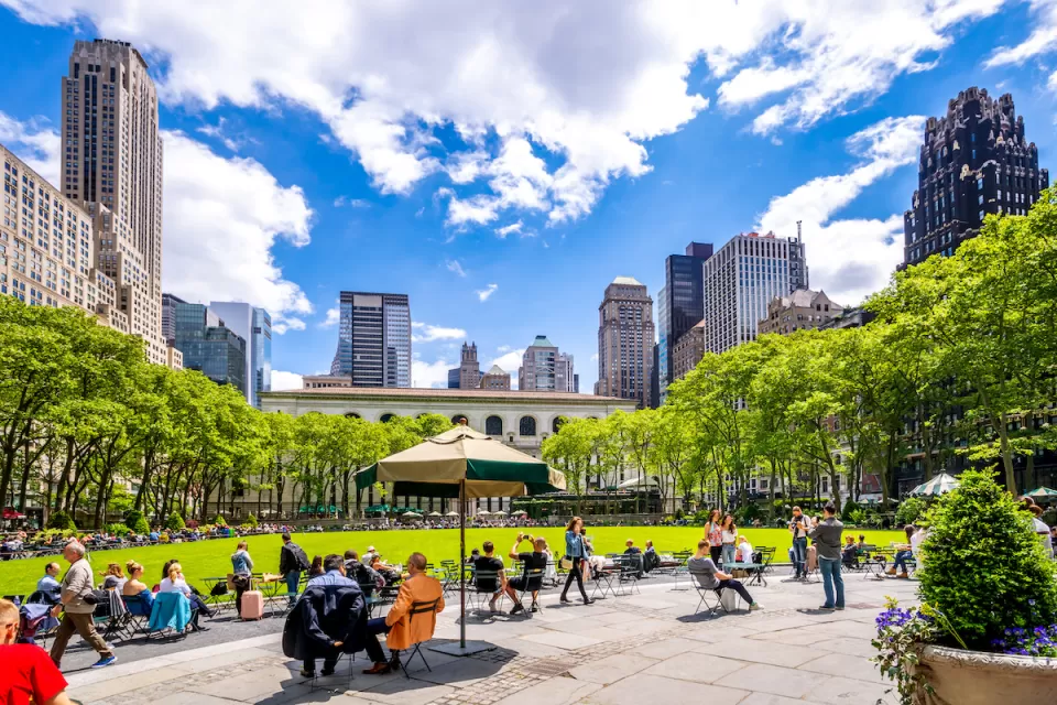 People sitting on lawn chairs in front of green meadow with New York City skyscrapers in background in Bryant Park, New York.